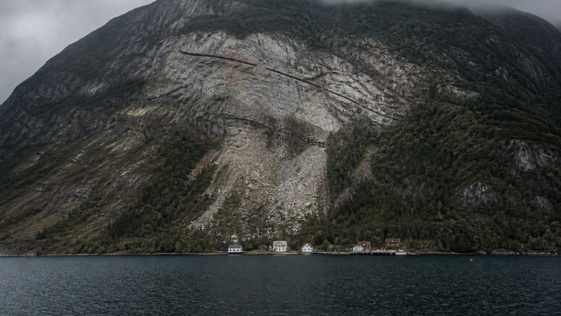 Bratt fjellside over norsk fjord med lang åpen sprekk og lyst utrasingssår under